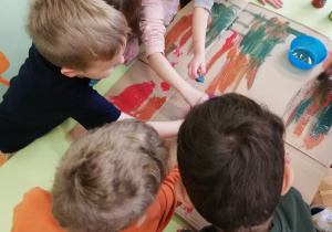 na zdjeciu dzieci przy stoliku malują farbami grubą tekturę kolorami jesieni - brązowo- zielono -czerwonymi